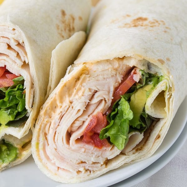 Two turkey wraps, cut in half, revealing turkey, lettuce, tomato, avocado, and sauce.