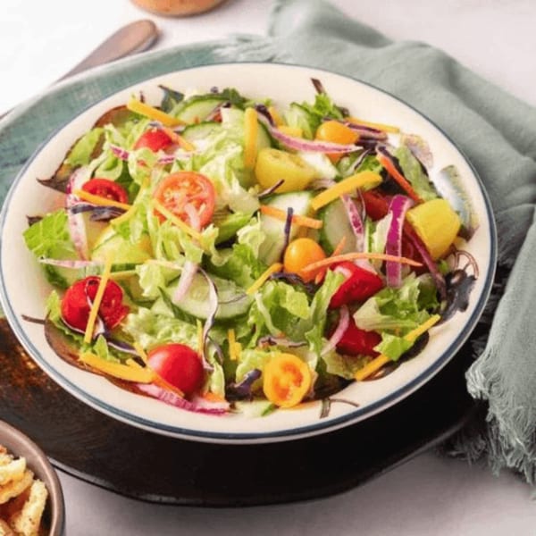 A fresh garden salad with lettuce, tomatoes, cucumbers, red onion, and shredded cheese.